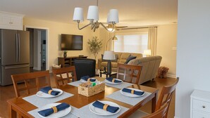 A dining area with a wooden table set for four, a kitchen with a refrigerator, and a living room with a sofa and a TV. - One-level Family Retreat I  Game Room I Bourbon Trail I King bed (Lebanon)