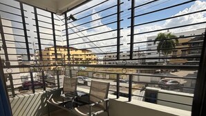 Un balcone con due sedie e un tavolo, ampie finestre e vista su edifici e una strada.