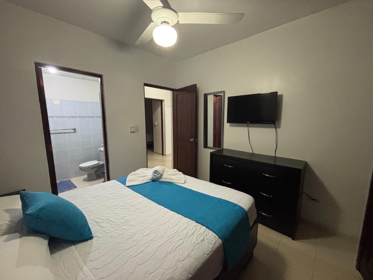 A bedroom with a bed, a dresser, a television, and a door leading to a bathroom.