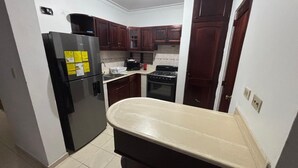 Una cucina compatta con pensili e basi in legno scuro, un frigorifero nero, un fornello e un lavello.