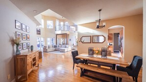 A spacious living area with a wooden floor, a dining table with chairs, a sofa, and a balcony with a railing. - Luxury Lakefront Retreat w Pool, Balcony, Firepit, Dock, Orlando, FL Sleeps 12 (Orlando)