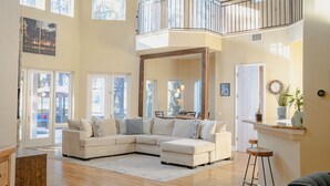 A spacious living area with a large L-shaped sectional sofa, a balcony with a railing, and a view of the outdoors. - Luxury Lakefront Retreat w Pool, Balcony, Firepit, Dock, Orlando, FL Sleeps 12 (Orlando)