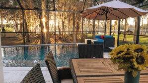 An outdoor pool area with a wooden table and chairs, a wicker sofa, and a large umbrella. - Luxury Lakefront Retreat w Pool, Balcony, Firepit, Dock, Orlando, FL Sleeps 12 (Orlando)
