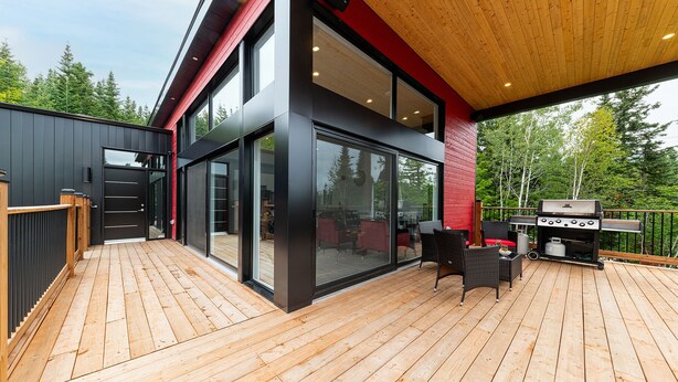 Una casa moderna con una terrazza, ampie porte scorrevoli in vetro e una zona barbecue.