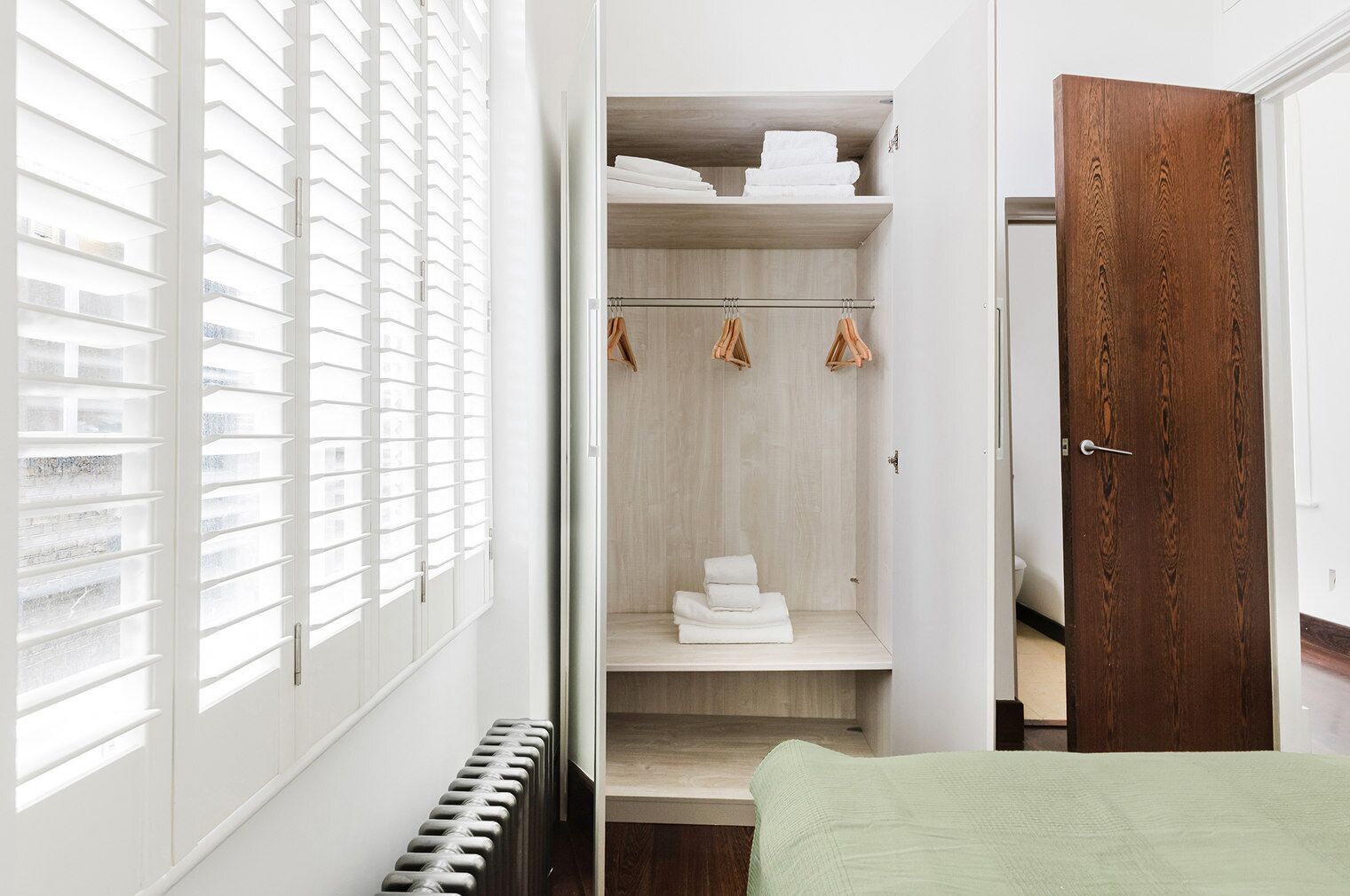 Ein begehbarer Kleiderschrank mit Holztür, Heizkörper und Fenster mit Jalousien.