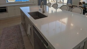 Une cuisine moderne dotée d’un grand îlot central, d’un four encastré et offrant une vue sur l’extérieur.