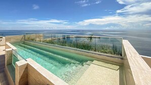 Una piscina cristalina con una barrera de vidrio, rodeada por una terraza de madera, con vista a una extensión de agua.