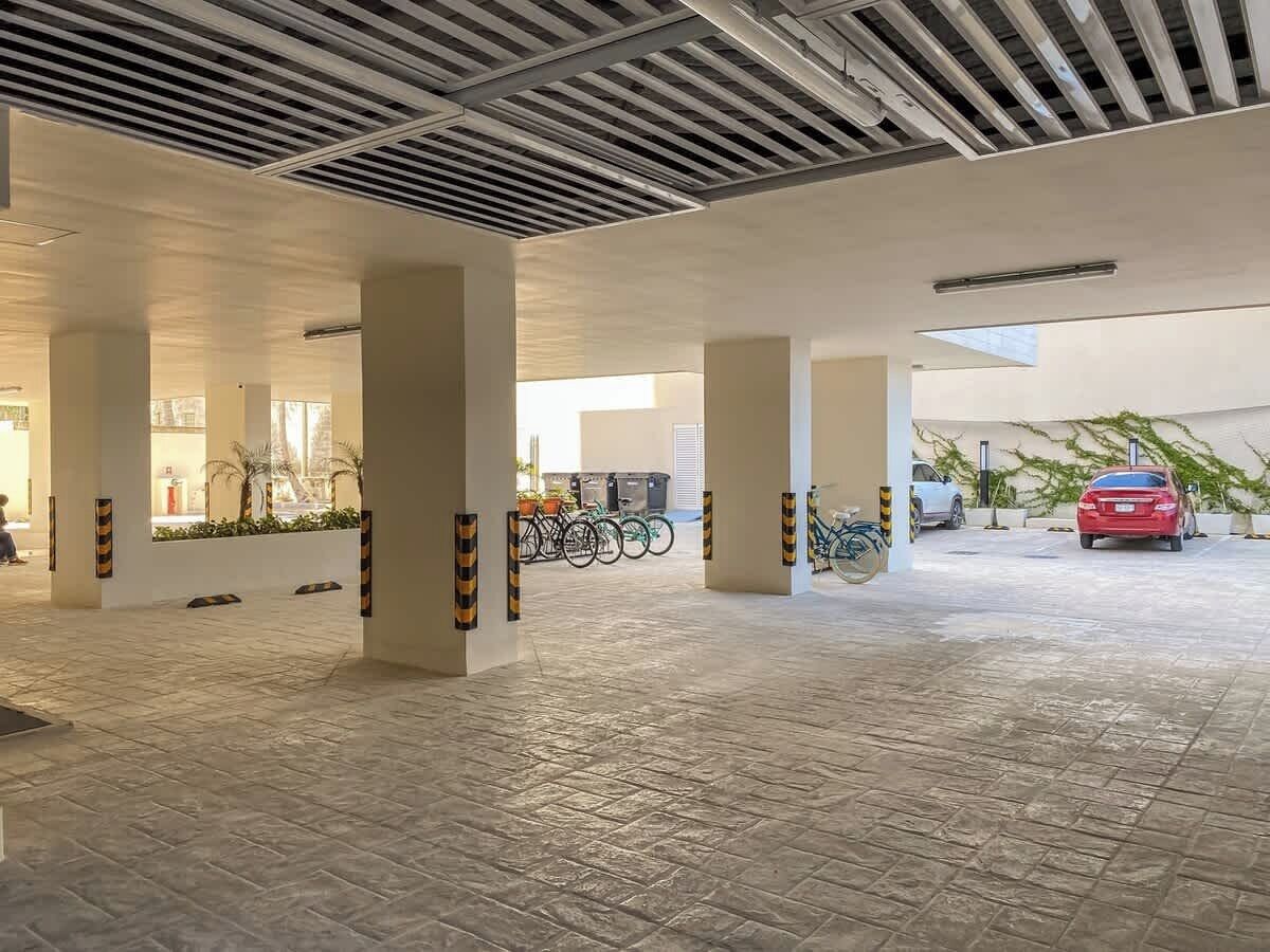 A spacious indoor parking area with a tiled floor, several columns, and a red car parked in the distance.