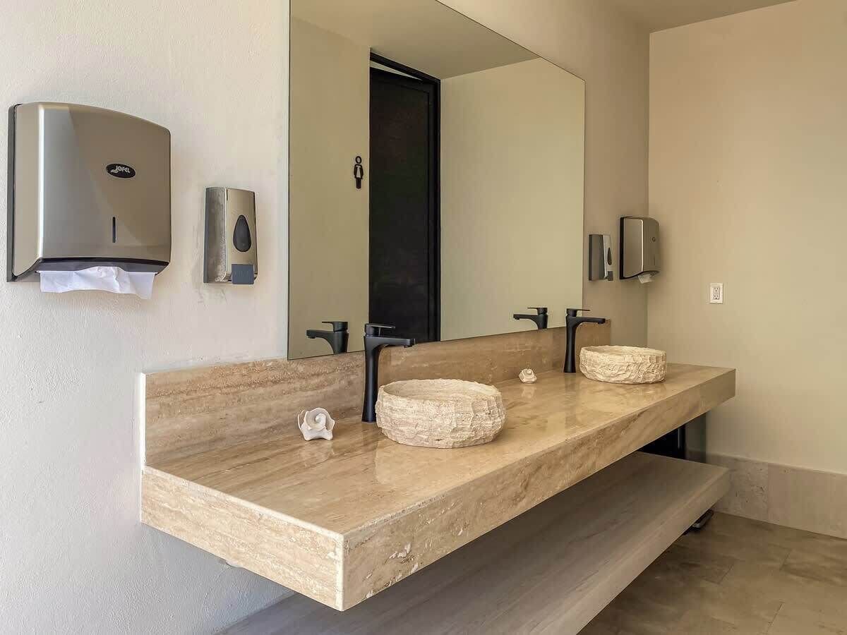 Un baño con dos lavamanos, un espejo y dos dispensadores de jabón.