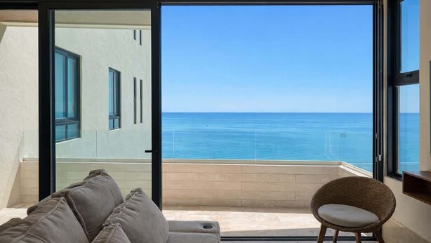 Un balcón con vista al mar, un sofá y una silla de mimbre.