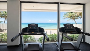 Two treadmills with digital displays, positioned in a room with large windows overlooking a beach. - Beachfront 3BR Puerto Morelos - Rooftop Pool (Puerto Morelos)