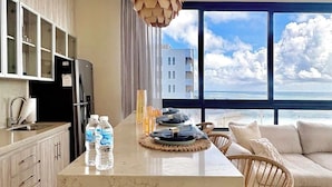 A modern kitchen with a marble island, a dining area with a view, and a large window. - Beachfront 3BR Puerto Morelos - Rooftop Pool (Puerto Morelos)