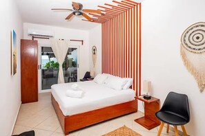 Een slaapkamer met een bed, een plafondventilator, een houten nachtkastje, een zwarte stoel en een muur met verticale strepen.