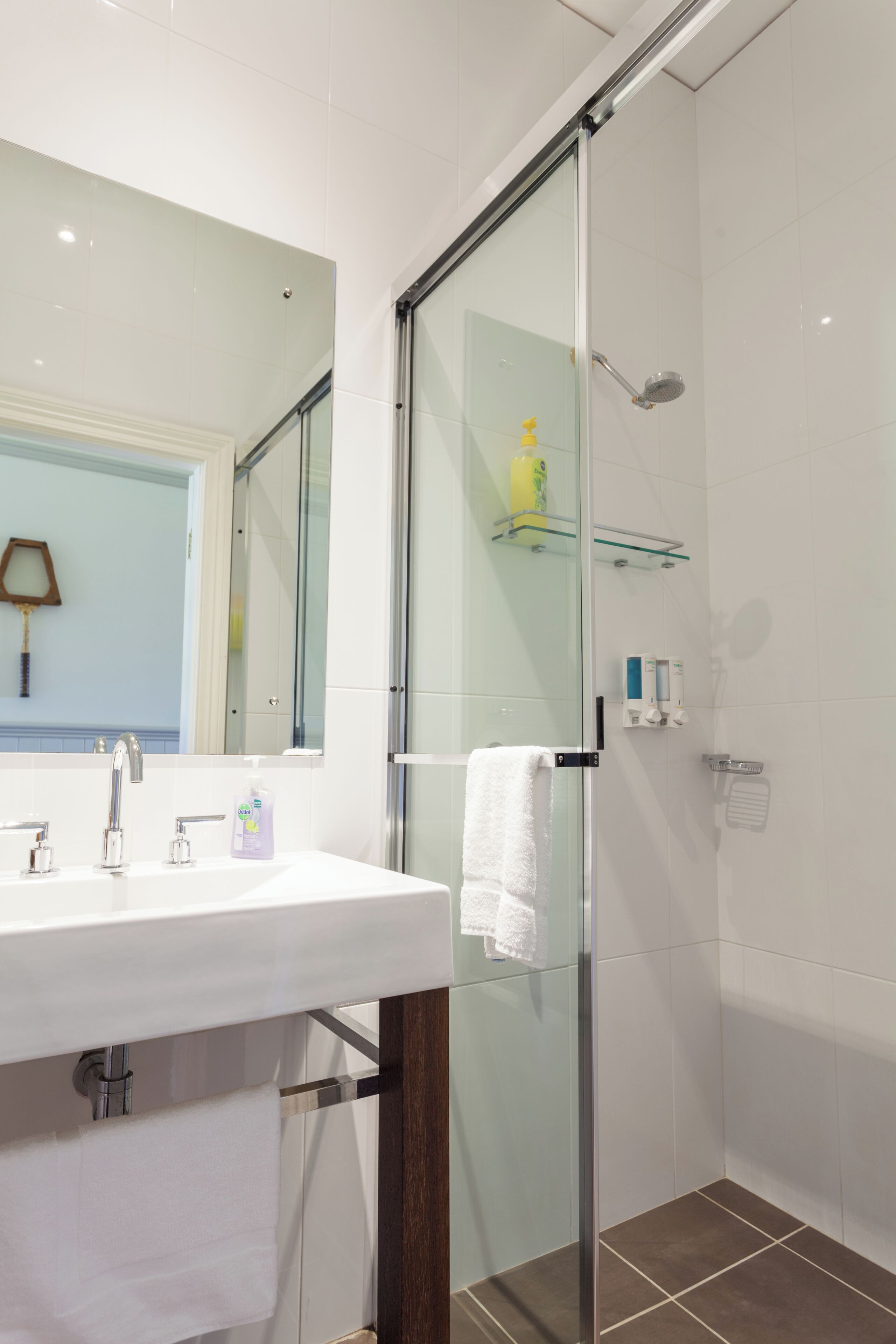 A modern bathroom with a glass shower enclosure, a white sink with a mirror, and a glass shelf above the sink.