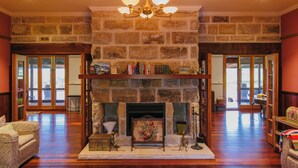 A spacious living room with a stone fireplace, wooden flooring, and a chandelier. - Hanging Tree Homestead - vineyard views, nature & farm animals. Pet-Friendly! (Pokolbin)