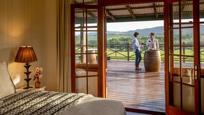 A room with a bed, a lamp, and a view of a balcony with two people holding wine glasses. - Hanging Tree Homestead - vineyard views, nature & farm animals. Pet-Friendly! (Pokolbin)