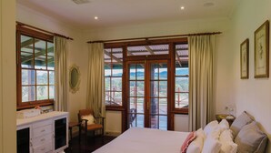 A bedroom with a large bed, a desk, and a chair. There are curtains on the windows, and a view of the outdoors is visible. - Hanging Tree Homestead - vineyard views, nature & farm animals. Pet-Friendly! (Pokolbin)