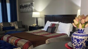 A hotel room with a bed, a sofa, a nightstand, a lamp, and a vase with flowers. - Cozy Studio near Universal (Orlando)