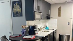 A compact kitchen with dark cabinets, a white countertop, and a small island. There are two chairs and a vase on the island. - Cozy Studio near Universal (Orlando)