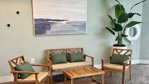A room with a wooden sofa set, two matching chairs, a small wooden coffee table, a large abstract painting, and a potted plant. - Cozy Studio near Universal (Orlando)