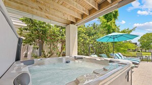 Een hottub onder een houten pergola met lounge fauteuils en een parasol.
