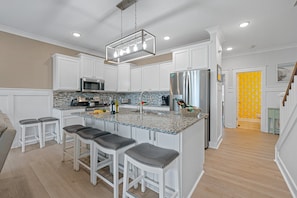 A modern kitchen with white cabinets, a stainless steel refrigerator, and a granite countertop. - 29 Sandcastle Court @ Folly Field Beach | 3D Projector | Pet Friendly | Lagoon Views (Hilton Head Island)