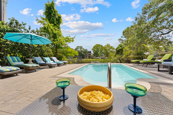 A pool area with lounge chairs, a bowl of chips, and a glass on a table. - 29 Sandcastle Court @ Folly Field Beach | 3D Projector | Pet Friendly | Lagoon Views (Hilton Head Island)