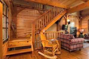 Ein Holzinnenraum mit Treppe, Schaukelstuhl, kariertem Sofa und Kamin.