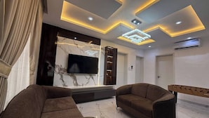 Een moderne woonkamer met een marmeren vloer, twee bruine banken, een flatscreen-tv en een uniek plafondontwerp met inbouwverlichting.