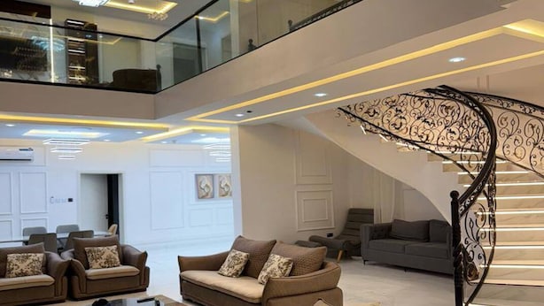 Een ruime woonkamer met een moderne trap en een hoog plafond met ingebouwde verlichting.