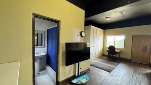 Una habitación con piso de madera, un televisor, un reloj y una ventana.