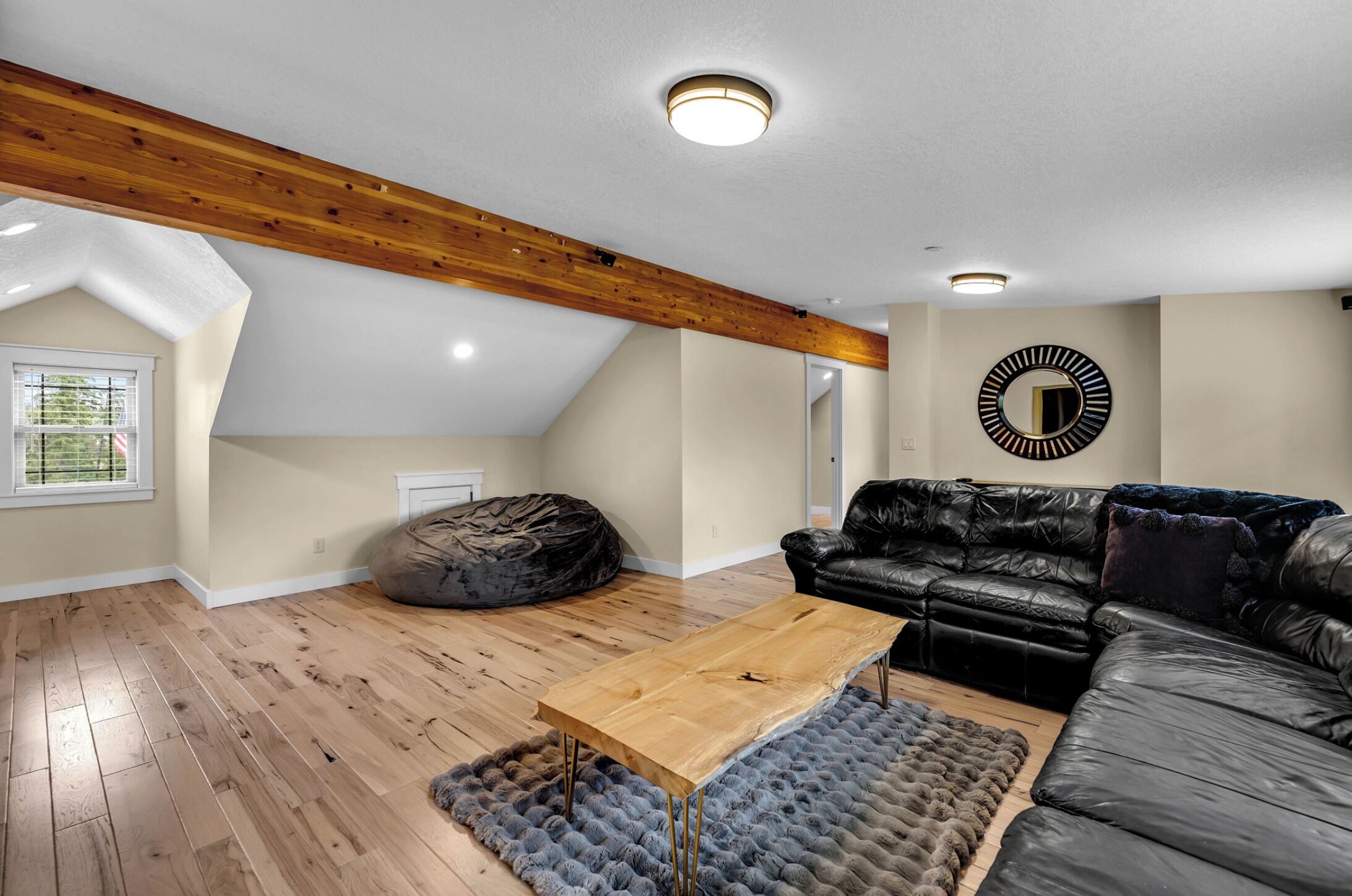 Un loft espacioso con techo alto, vigas de madera a la vista, un sofá de cuero negro, una mesa de centro de madera y un espejo redondo en la pared.