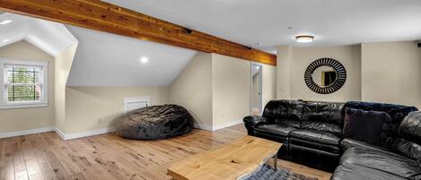 Un loft espacioso con techo alto, vigas de madera a la vista, un sofá de cuero negro, una mesa de centro de madera y un espejo redondo en la pared.