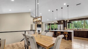 Une cuisine moderne dotée d’un grand îlot central, d’une table à manger en bois et de luminaires suspendus.