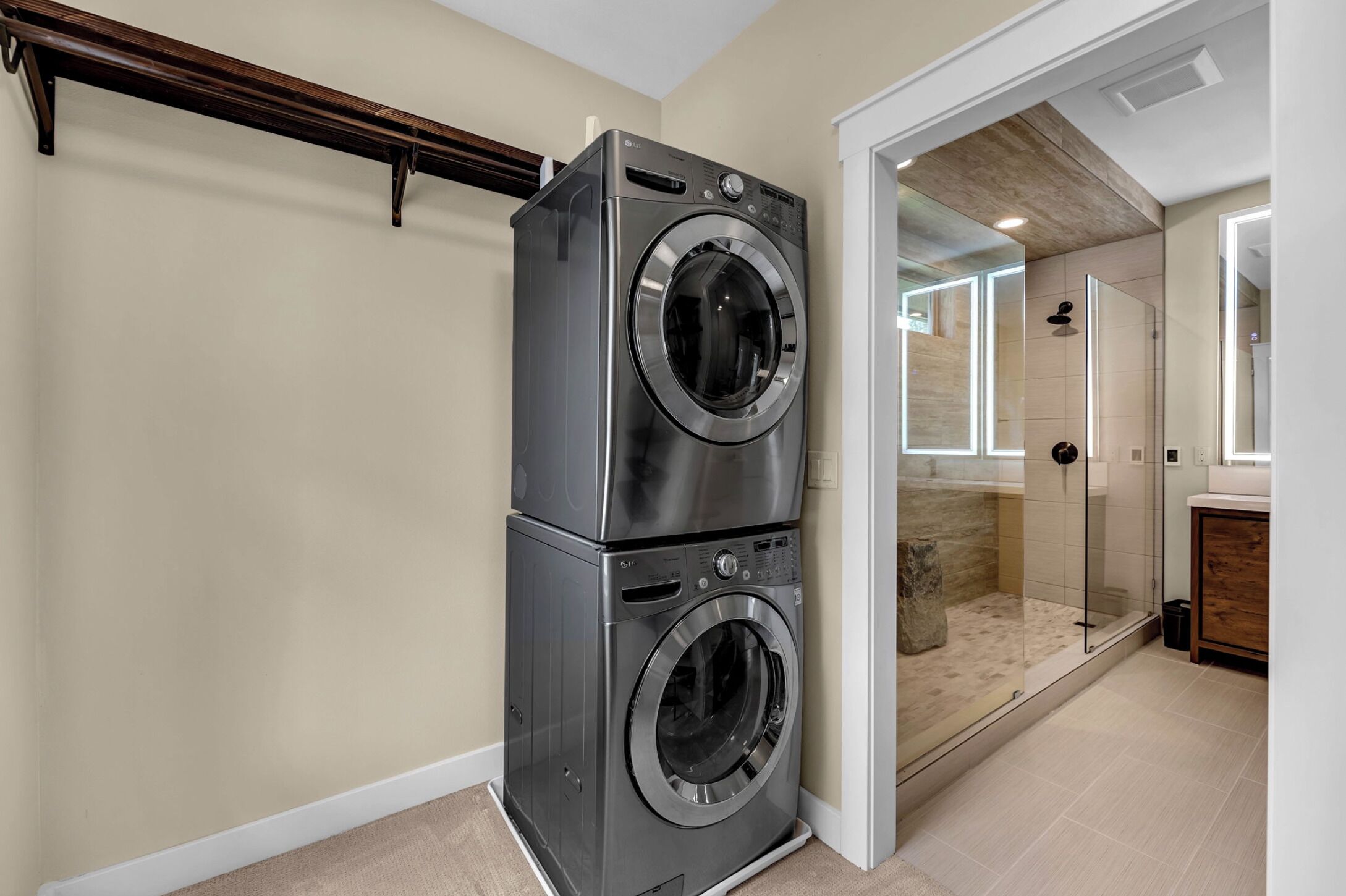 Un espace buanderie avec des lave-linge et des sèche-linge superposés, une cabine de douche en verre et un banc en bois.