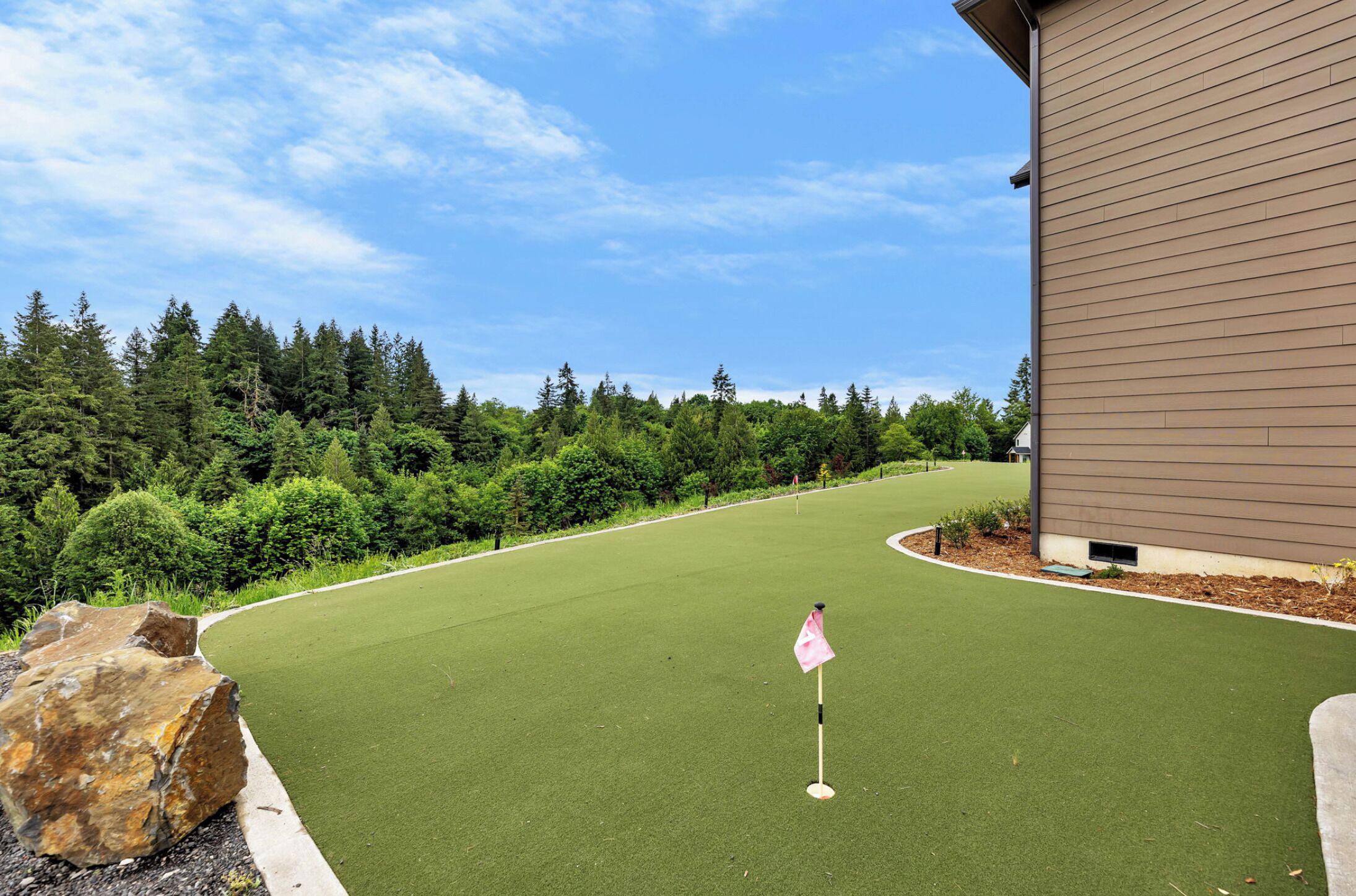 A golf course with a putting green, a flag, and a building in the background.