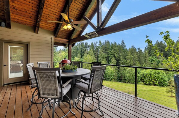 A wooden deck with a round table and four chairs, overlooking a forested area. - The Ridgefield Grand Estate – Luxury on 3 Levels (Ridgefield)