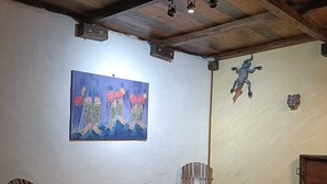 Een kamer met een houten plafond, een schilderij aan de muur, een houten tafel, twee stoelen en een rode bed.