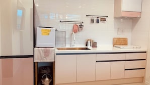 Una cucina moderna con mobili bianchi, un lavello in acciaio inossidabile, un frigorifero bianco e un forno Samsung.