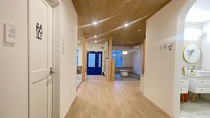 A hotel corridor with a wooden ceiling, a blue door, and a bathroom with a sink and mirror. - TINY HOTEL YADORIGI KAMIGOTO (Shinkamigoto)