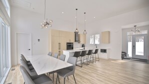 A modern kitchen with a central island, a dining area with a large table and chairs, and a spacious living area with a large window.
