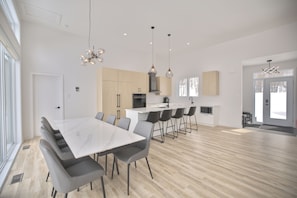 A modern kitchen with a central island, a dining area with a large table and chairs, and a spacious living area with a large window. - Modern Chalet in Bel Air Resort Tremblant (La Conception)