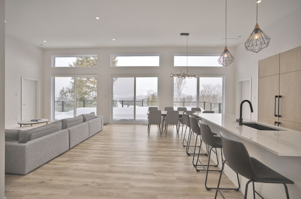 A modern kitchen with a large island, bar stools, and a view of the outdoors. - Modern Chalet in Bel Air Resort Tremblant (La Conception)