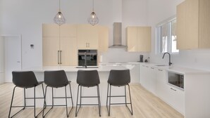 A modern kitchen with a central island, four bar stools, pendant lighting, and a large window.