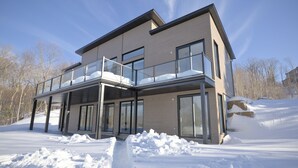 A modern two-story house with a balcony, large windows, and a snowy landscape.