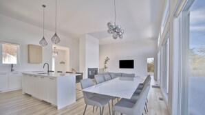 A modern kitchen with a central island, a dining area with a long table and chairs, and a large window providing natural light.