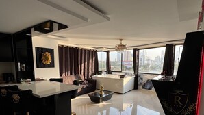 Un salon moderne doté d’un îlot central, d’un canapé, d’une table basse et offrant une vue sur la ville grâce à de grandes fenêtres.