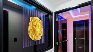 Un couloir moderne agrémenté d’une sculpture de lion, de portes en verre et d’un plafond éclairé en bleu.