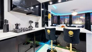 Une cuisine moderne avec des meubles de couleur noire, un plan de travail blanc et deux tabourets de bar ornés de détails dorés.