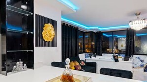 Un salon moderne avec une table basse en verre, un lustre et une vue sur la ville grâce à de grandes fenêtres.